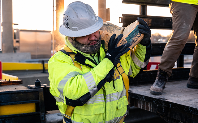 Worker in safety gear lifts bag from truck at site.