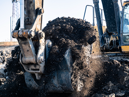 Excavator lifts dark soil with bucket