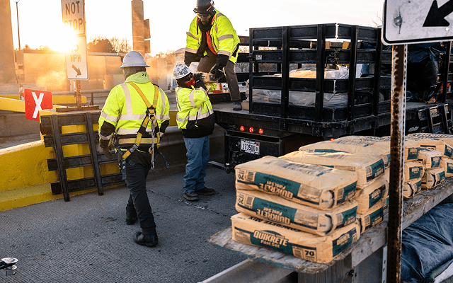 Workers in safety gear unload Quikrete bags from truck.