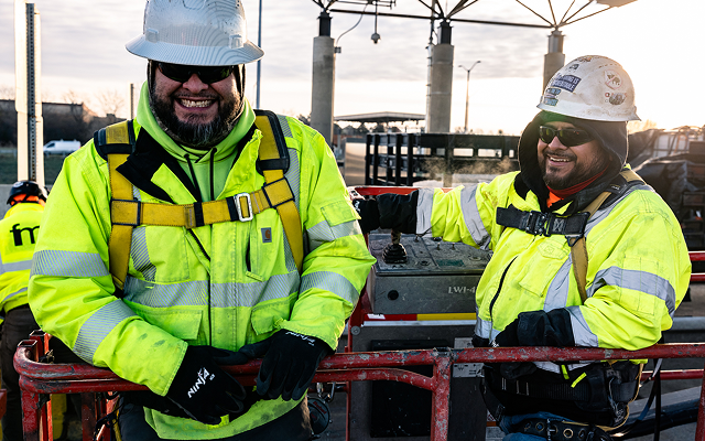 Two smiling construction workers in safety gear at job site.