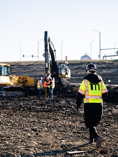 Workers in safety gear use machinery at dirt site