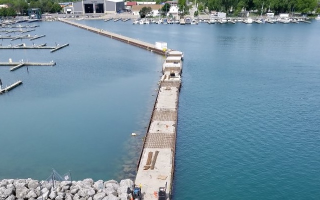 Aerial view: concrete pier under construction, marina and boats.