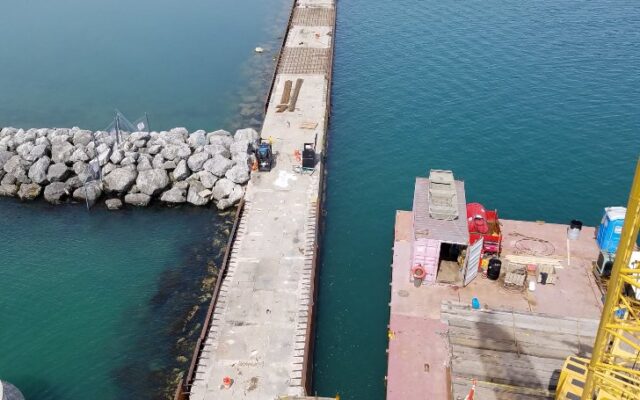 Aerial view: pier under construction extends into water near marina.