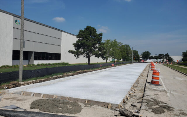 New concrete road curing, orange barrels line center of road.