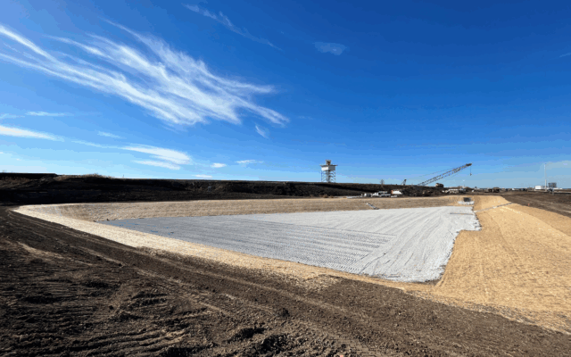 White geotextile covers ground; crane and tower in background.