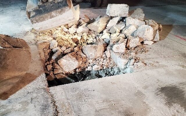 A bucket lifts concrete chunks out of the roadway during nighttime roadwork.