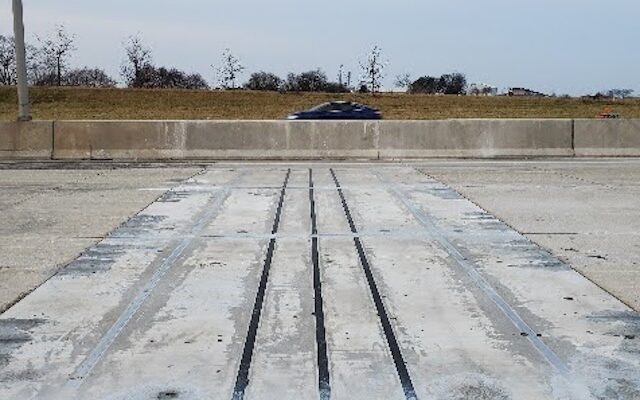 Grooved concrete road, barrier, and cloudy sky in background.