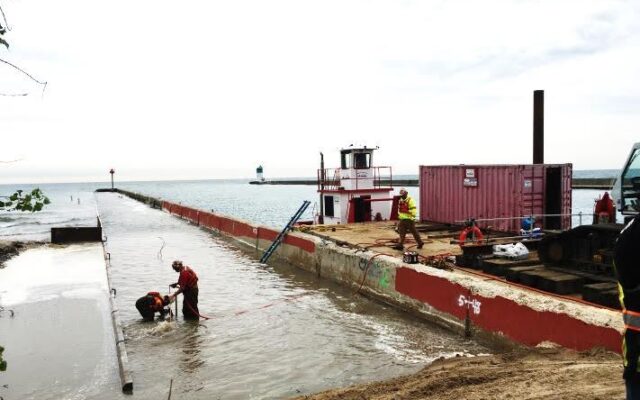 Workers in safety gear repair pier pipe near barge