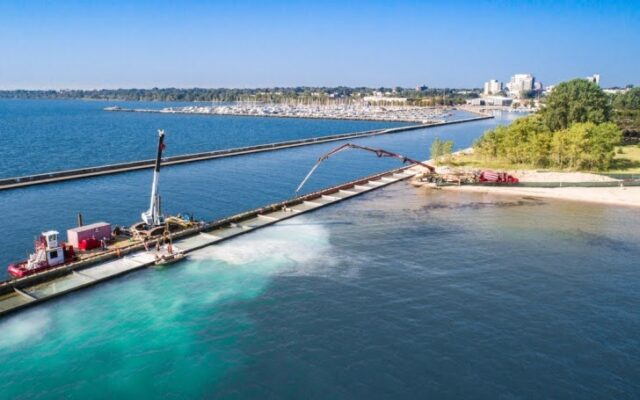 Aerial view: barge present and equipment operating in the water with marina in the distance