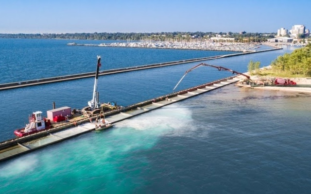 Construction barge with workers by a pier; marina and city behind.