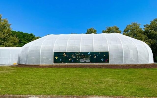 White mesh Butterfly House on lawn, trees and blue sky.