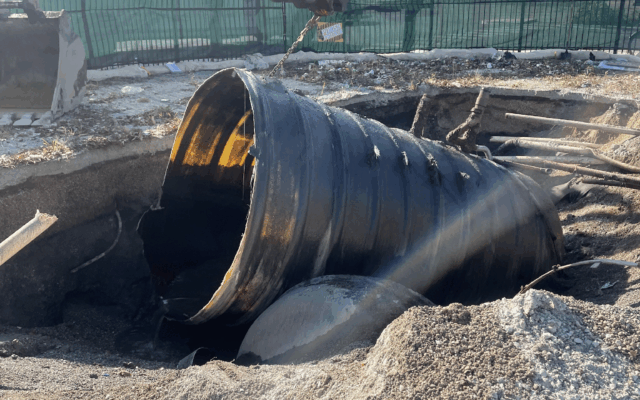 Heavy machinery lifts up large metal pipe near road.