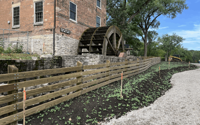 Large waterwheel on brick building, with fence and path.