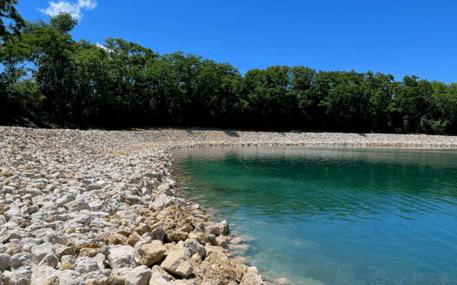 Turquoise water, white rocks, green trees, bright blue sky.