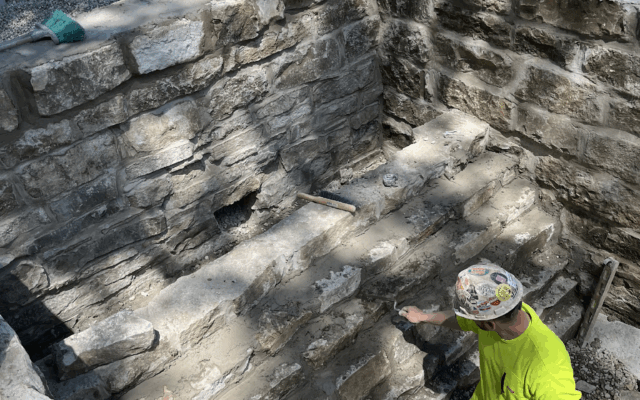 Worker in yellow shirt applies mortar to outdoor stone wall.