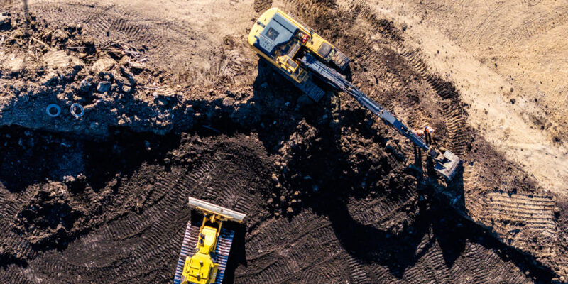 Aerial view: yellow excavator digging, bulldozer on dark soil.